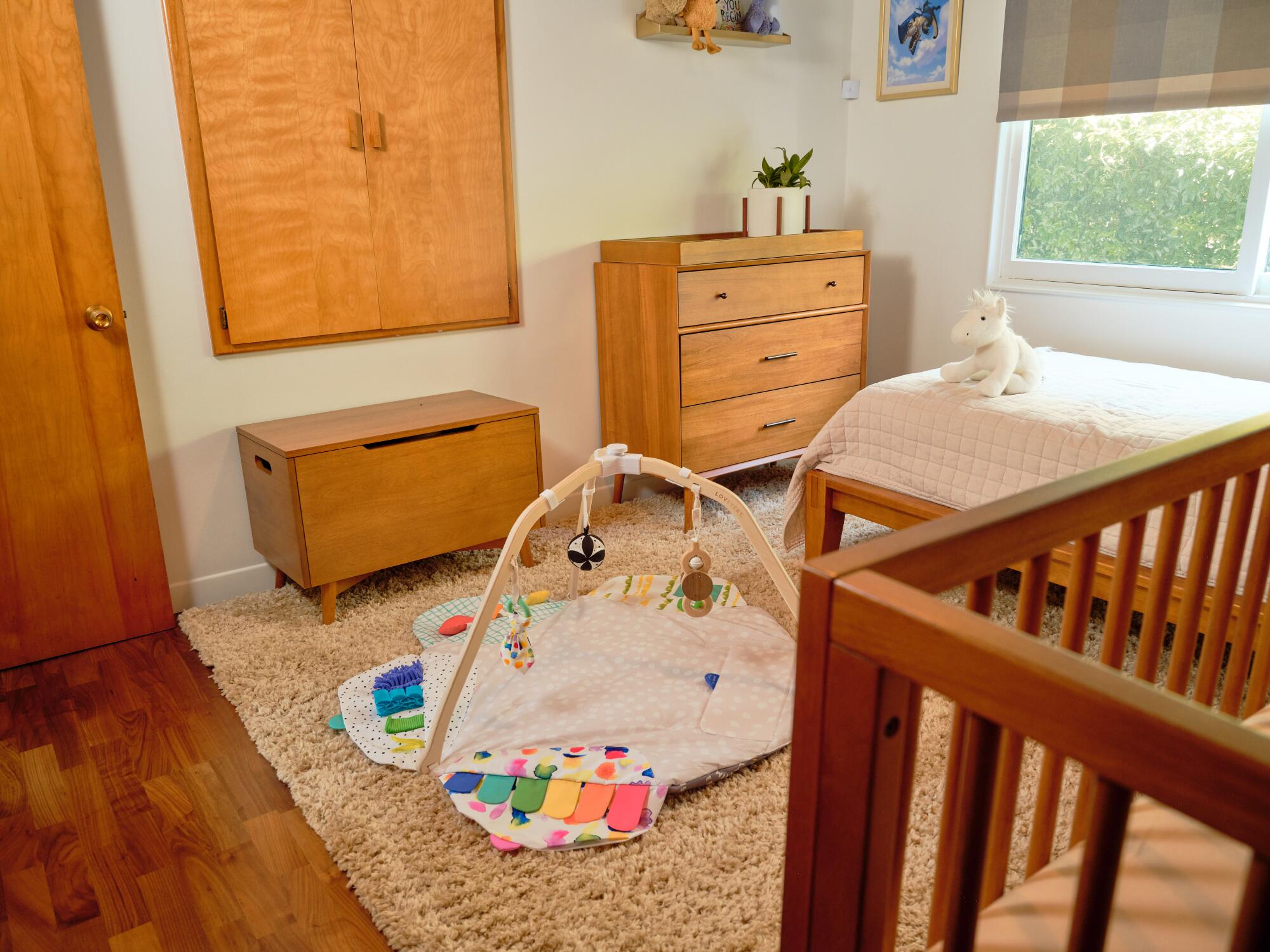 A crib and baby mat in the guest room filled with light wood furniture.