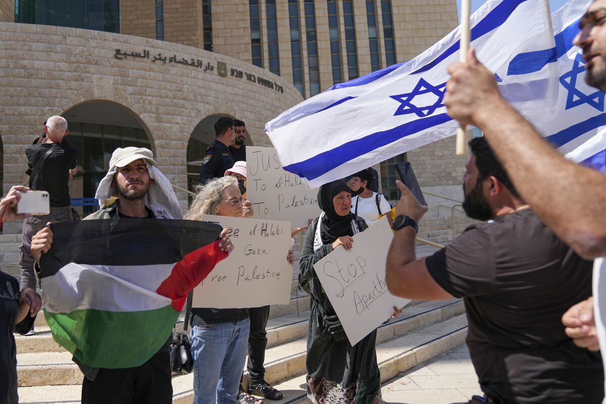 Supporters of Mohammed el-Halabi hold a Palestinian flag and placards as protesters wave Israeli flags, outside the district court in the southern Israeli city of Beersheba, Wednesday, June 15, 2022. The court found the Gaza aid worker guilty of several terrorism charges. El-Halabi, who was the Gaza director for the Christian charity World Vision from 2014 until his arrest in 2016, was accused of diverting tens of millions of dollars to the Islamic militant group Hamas that rules the territory. Both el-Halabi and World Vision have denied any wrongdoing, and an independent audit in 2017 also found no evidence of support for Hamas. (AP Photo/Tsafrir Abayov)