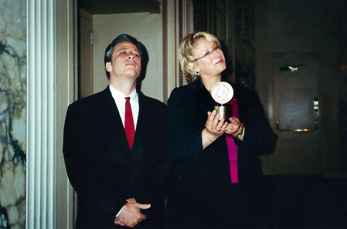 A man and a woman in humorous poses with a Peabody Award.