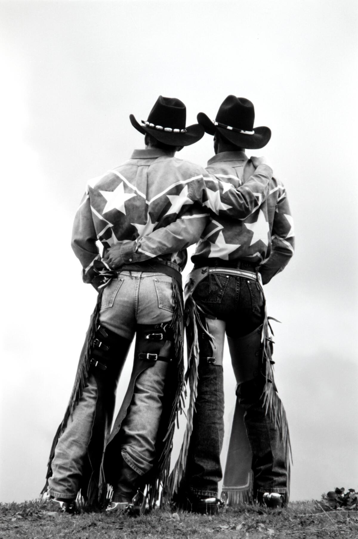 Two cowboys standing side-by-side with arms wrapped around each other. 