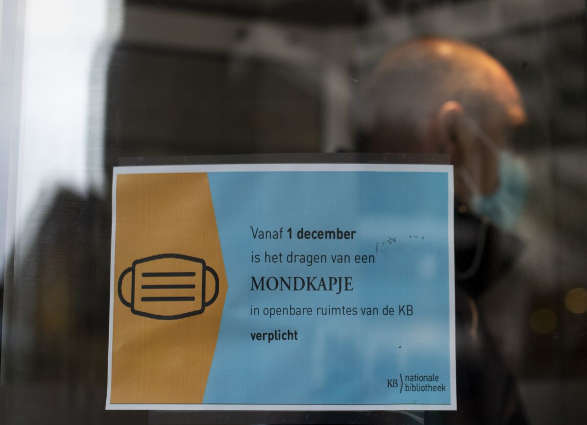 A man entering the national library in The Hague, Netherlands, Tuesday, Dec. 1, 2020, passes a sign informing visitors to wear mandatory face masks. Wearing face masks in publicly accessible indoor venues such as libraries, museums became obligatory in the Netherlands on Dec. 1, 2020, when a new temporary law underpinning existing government coronavirus restrictions came into force. (AP Photo/Peter Dejong)