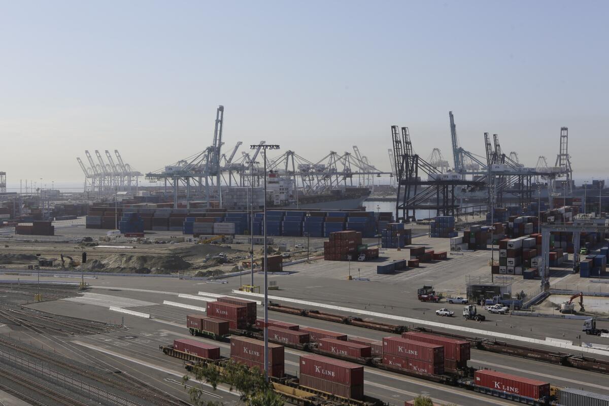 Shipping containers aboard rail cars stand against a backdrop of cargo cranes