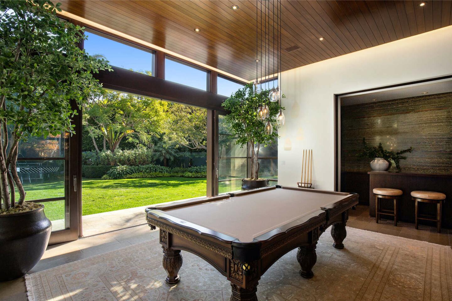 The billiards room with a pool table and glass wall overlooking trees and lawn.