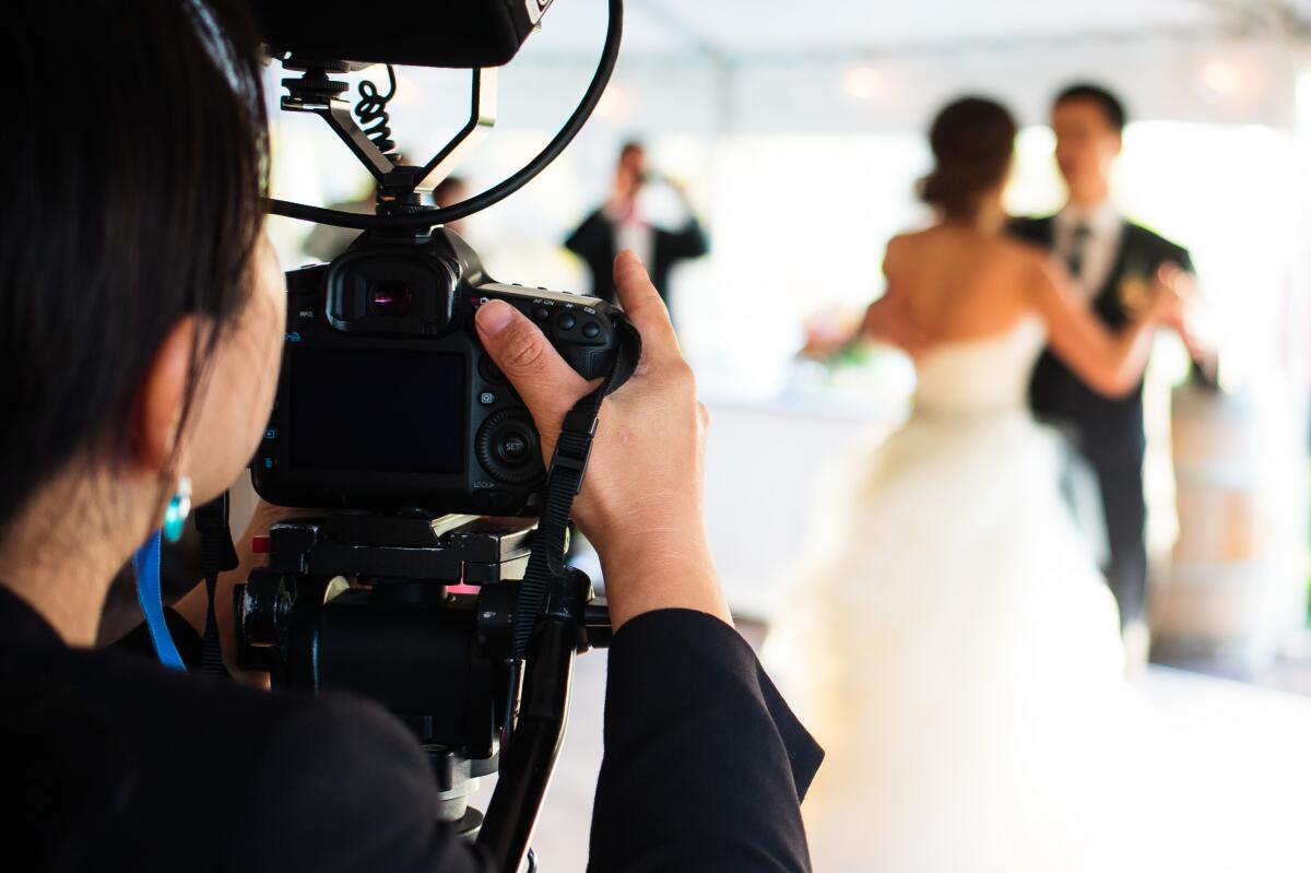 A woman looks through a camera at a couple dancing at a wedding