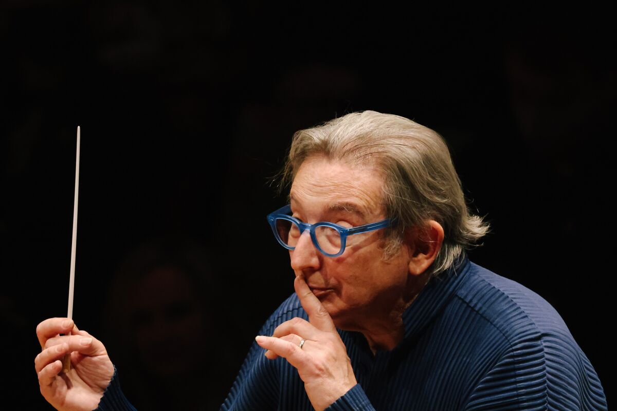 Michael Tilson Thomas, in a blue shirt, presses a finger to his lips while he leads the L.A. Phil