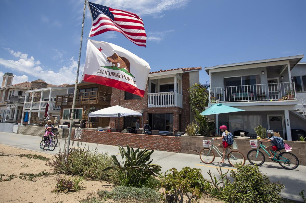 People ride bikes past a flagpole in front of a row of houses.