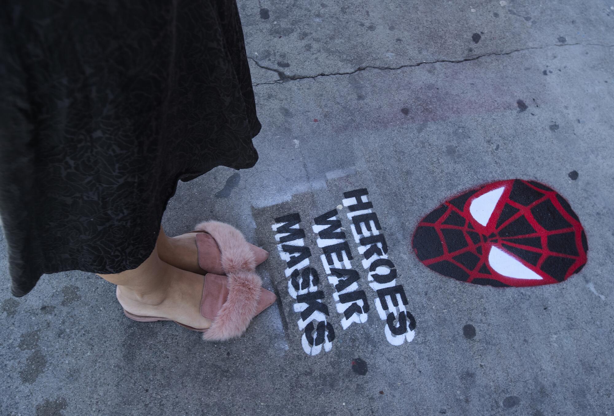 A passerby checks out a Spider-Man themed "Heroes Wear Masks" stencil along Traction Avenue near 3rd Street in Los Angeles.