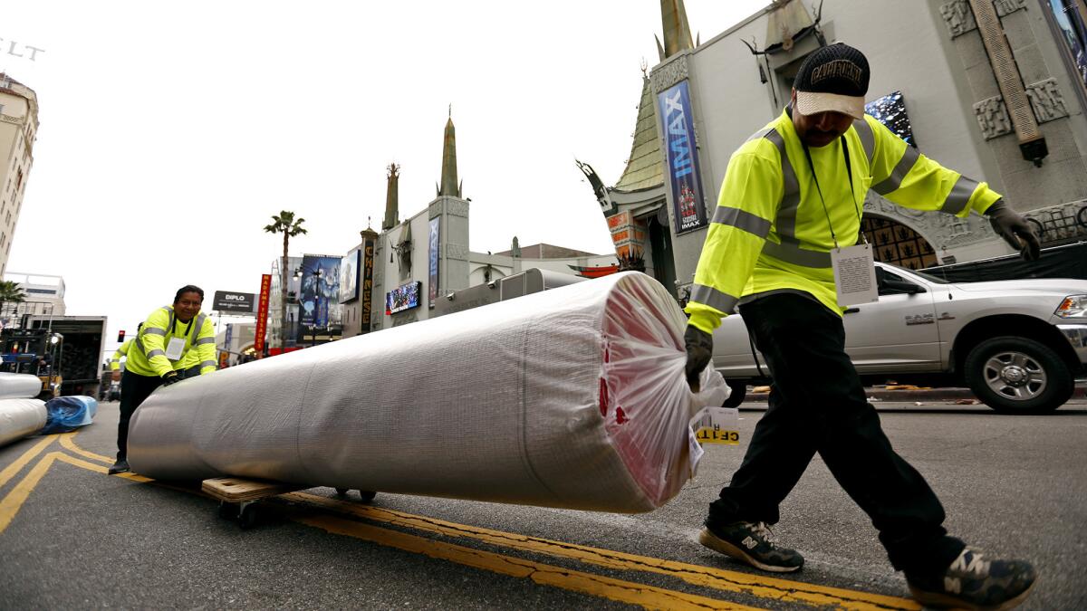 Installers carry the red carpet down Hollywood Boulevard. (Al Seib / Los Angeles Times)