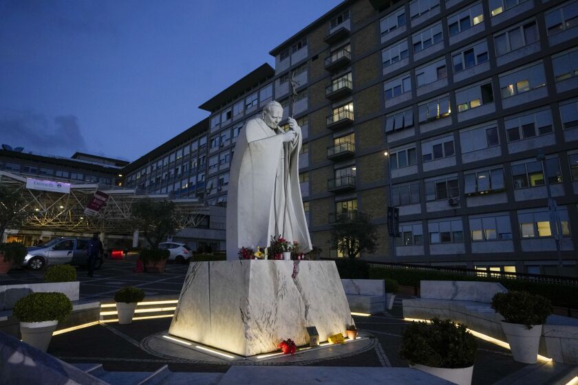 A statue of late Pope John Paul II is backdropped by the rooms on the top floor normally used when a pope is hospitalized at the Agostino Gemelli hospital, in Rome, Friday, March 31, 2023. Pope Francis is expected to be discharged on Saturday from the Rome hospital where he is being treated for bronchitis as his recovery proceeds in a "normal" way, even had pizza for dinner and will be in St. Peter's Square for Palm Sunday Mass, the Vatican said. (AP Photo/Andrew Medichini)