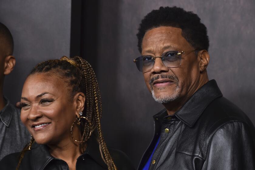 Linda Mathis smiling in braids and large hoop earrings with Judge Mathis looking serious in tinted glasses and leather jacket