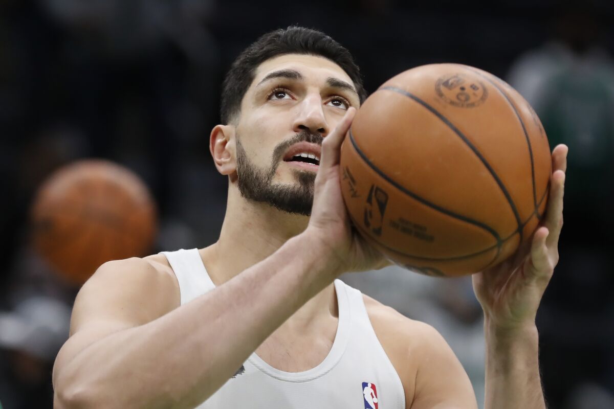 Beyaz kolsuz bluz giymiş koyu saçlı bir adamın iki elinde de basketbol topu tutarken yukarı bakarken baş ve omuz görünümü. 