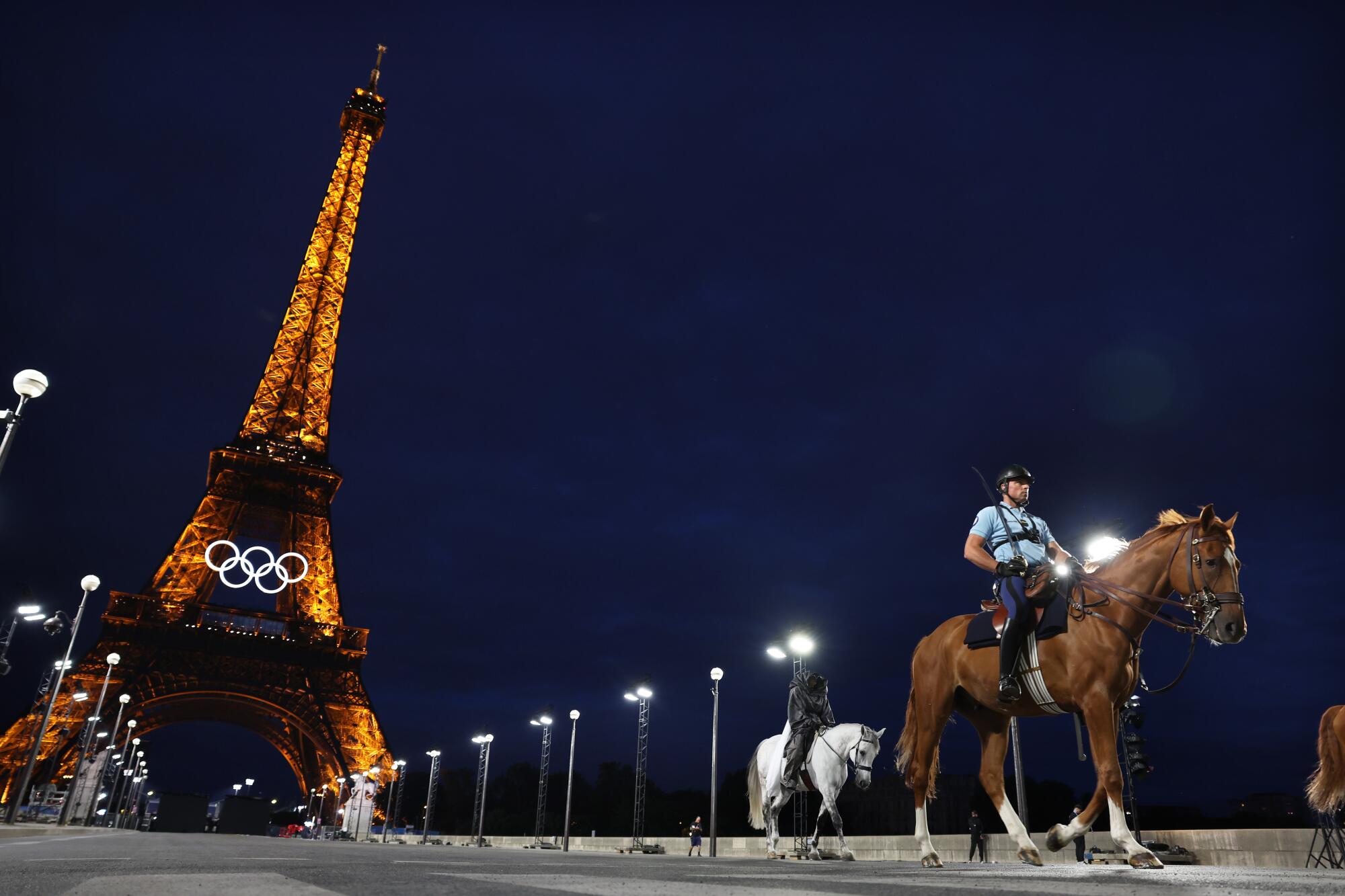 Mounted police officers ride near the Eiffel Tower at night.