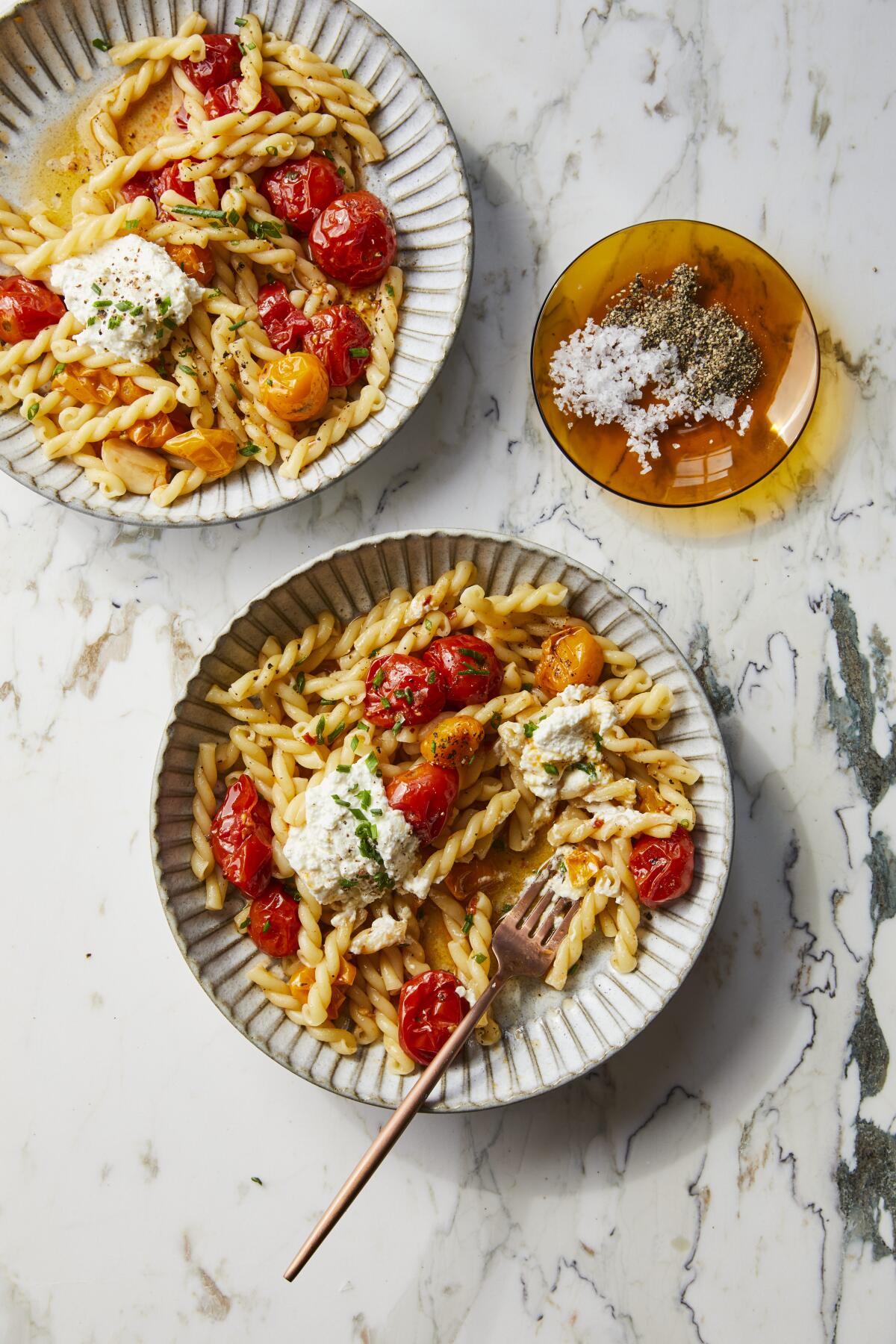 Overhead view of two plates with gemelli pasta and small whole charred tomatoes.