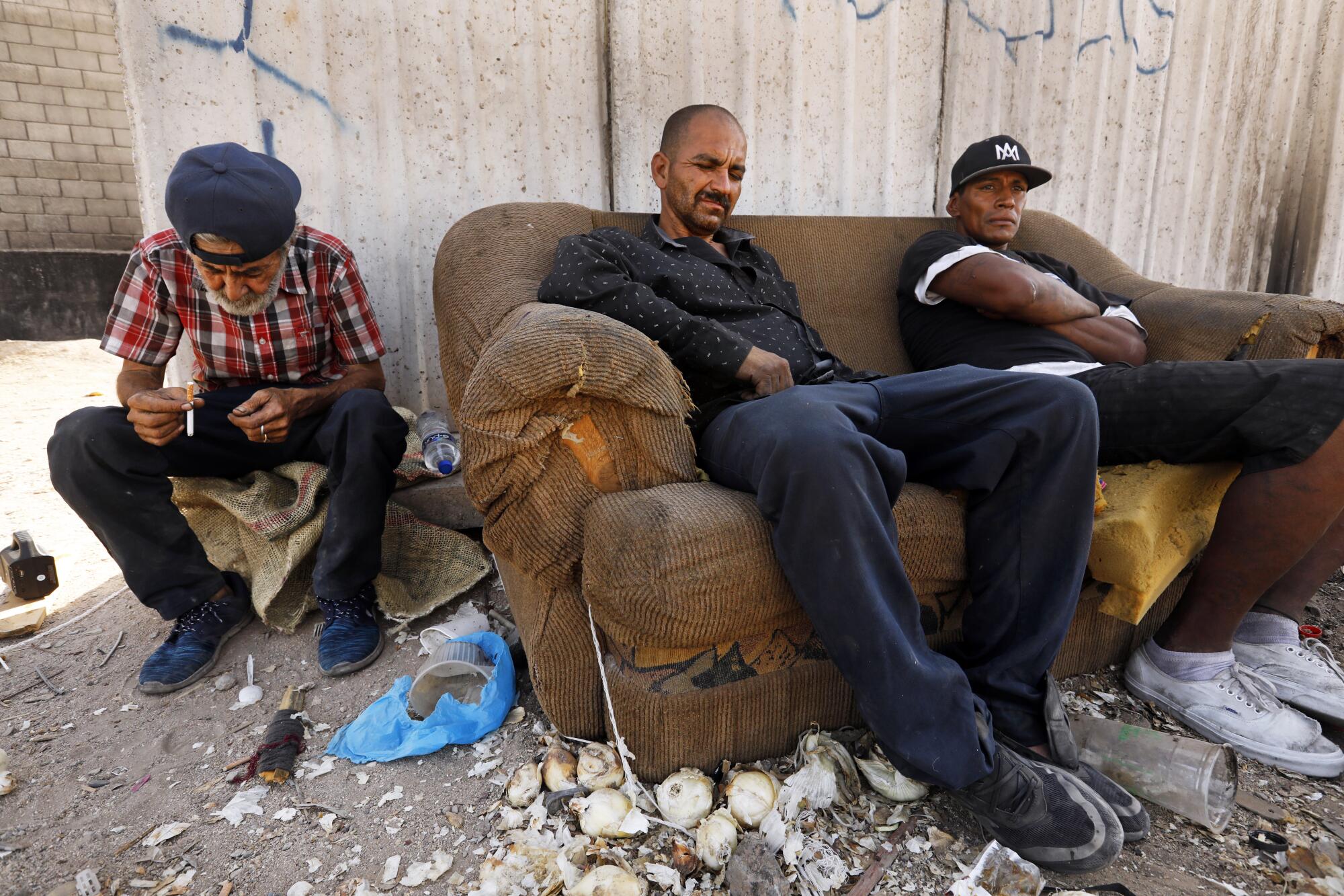 Dos hombres están sentados en un sofá junto a otro hombre, con escombros en el suelo 