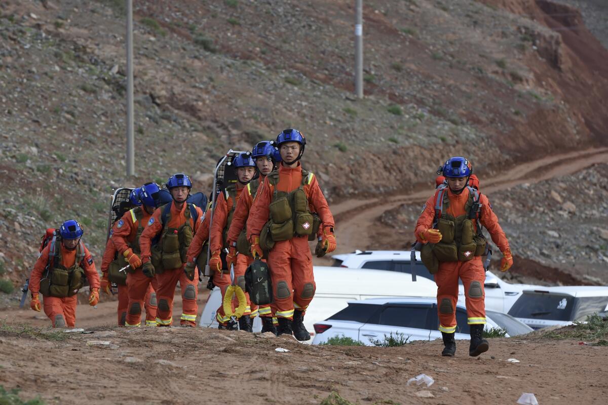 A line of people in helmets and outdoors rescue gear walk amid barren hills.