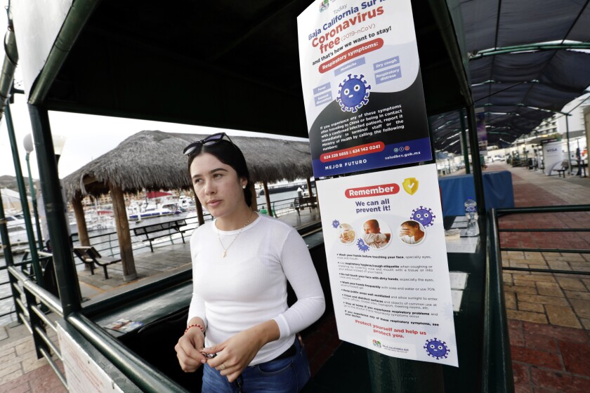 At the docks in Cabo San Lucas, a sign reads: "South Baja California is free of coronavirus and that's how we want to stay!" Lituania Casena Guerena, 18, works greeting cruise ship visitors, but was only told to start wearing gloves a week ago.