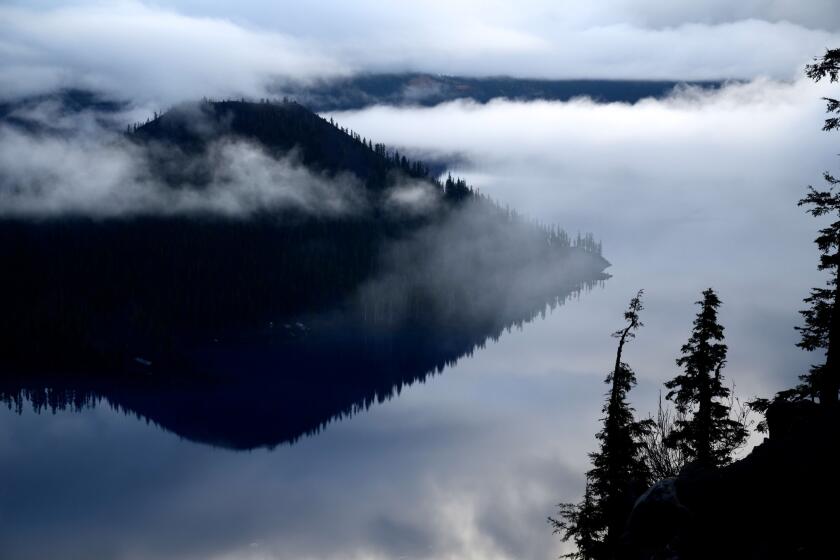 Wizard Island sits near the edge of famously blue Crater Lake in Oregon. The Cleetwood Trail, on the far caldera slope, hidden by mist, is the only way down to water's edge, and it's only open in warmer months.