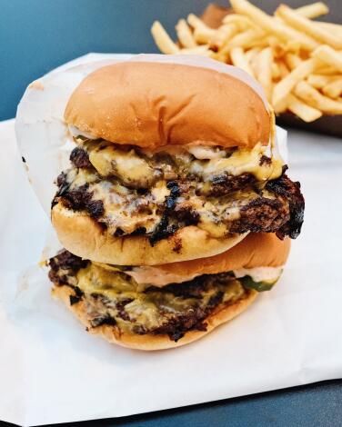 Two double cheeseburgers stacked from The Win-Dow, a smashburger walk-up window in Hollywood. Fries are in the background.