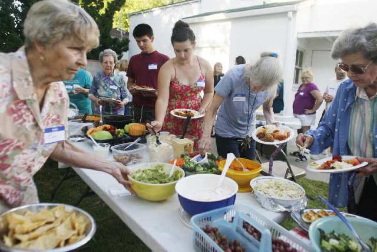 Sophie Wiegand, 13, center, and other church members and residents grab some food during a potluck dinner, which took place at Little White Chapel Christian Church in Burbank.