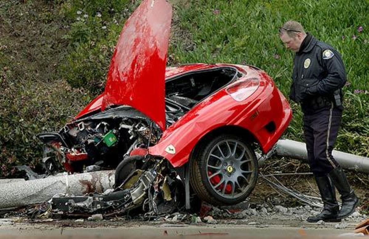 A Newport Beach police officer surveys wreckage of a Ferrari that split in half after hitting a pole on Jamboree Road. One man was killed, a woman was injured and another man was arrested in connection with the crash.