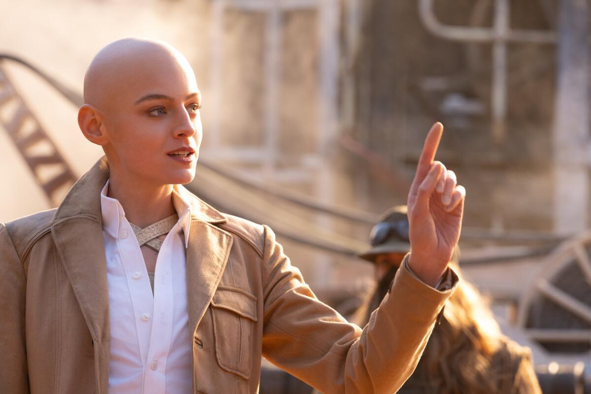 A bald woman raises an evil finger.