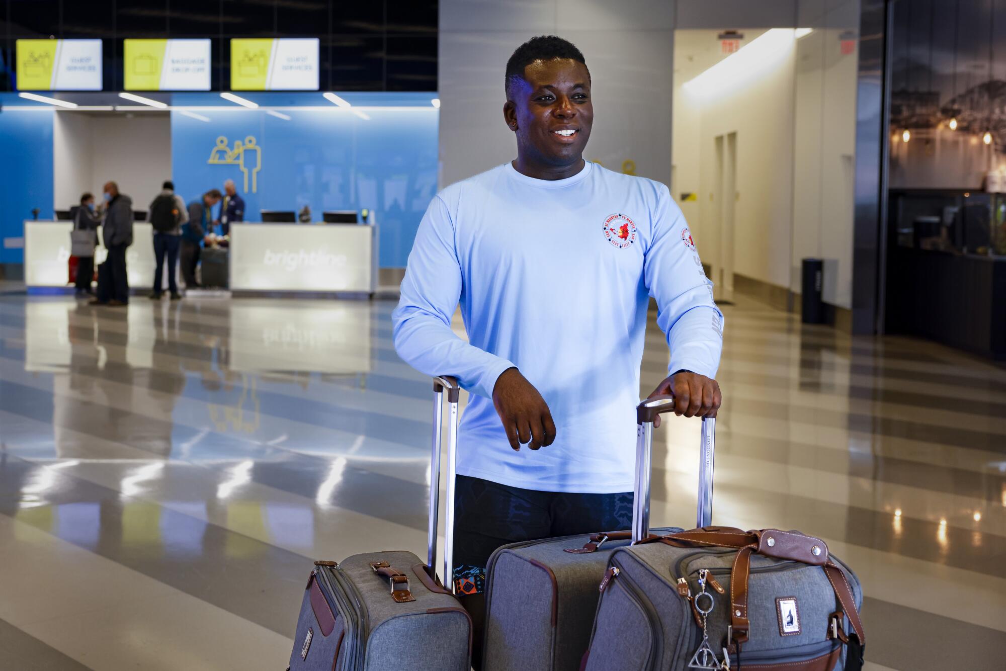 A man in a light blue long-sleeved shirt smiles as he stands with suitcases