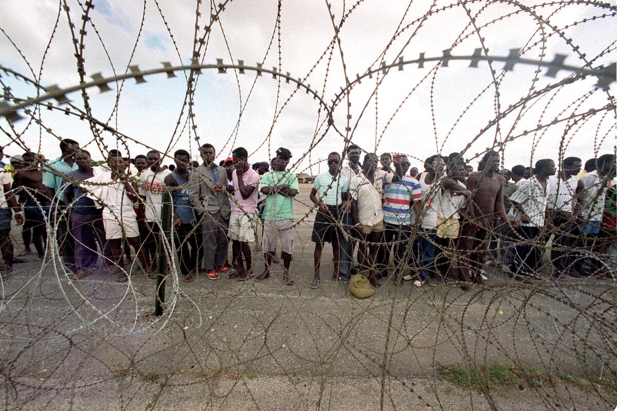 Haitian refugee men stand behind razor wire
