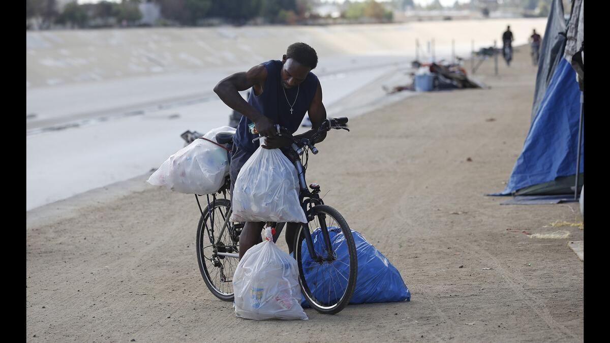 A man readies his belongings and bags of cans at a homeless encampment along the Santa Ana River trail in Fountain Valley.