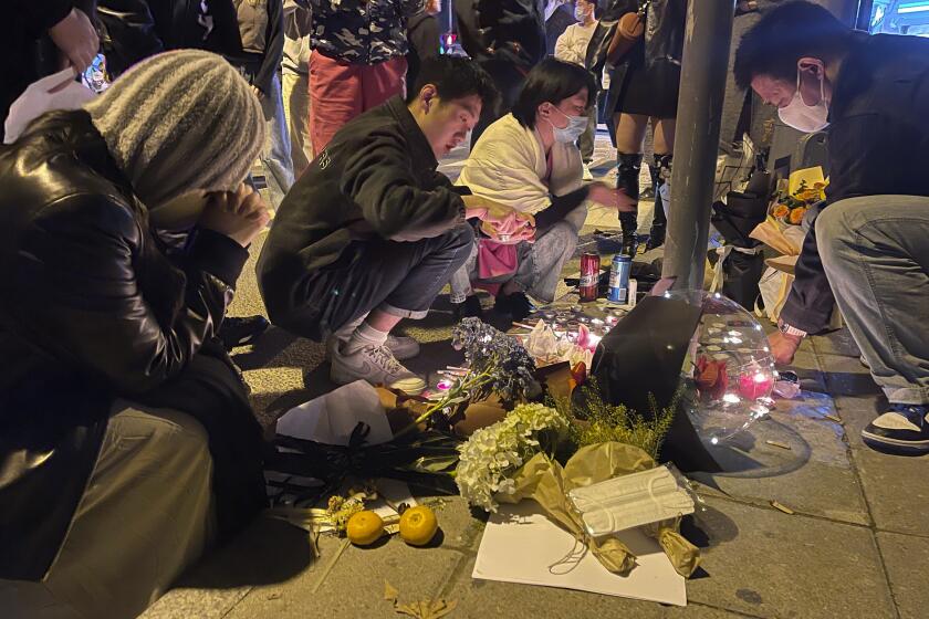 Residents mourn for the victims of a recent deadly fire at a residential building in Urumqi city at a road sign of the Middle Wulumuqi Road or Middle Urumqi Rd in Shanghai, China Saturday, Nov. 26, 2022. Protests against China's restrictive COVID-19 measures appeared to roil in a number of cities Saturday night, in displays of public defiance fanned by anger over a deadly fire in the western Xinjiang region. (Chinatopix Via AP)