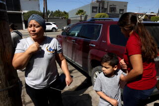 A woman in a gray shirt stands next to another woman, in a red shirt, holding the hand of a boy
