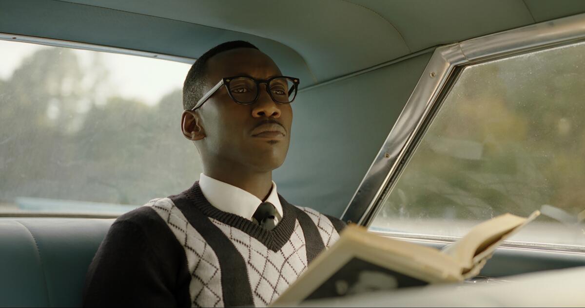 Mahershala Ali sits in the back seat of a car holding an open book in a scene from "Green Book" (2018).
