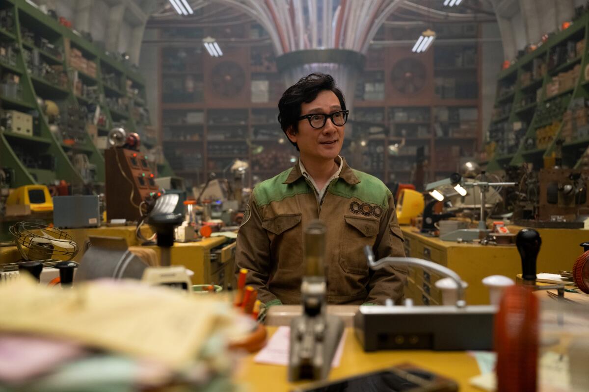 Ke Huy Quan as O.B. in a jumpsuit surrounded by shelves of various gadgets