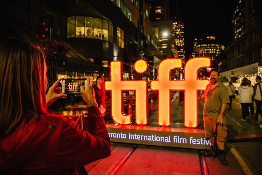 A man has his photo taken next to the TIFF, Toronto International Film Festival, sign