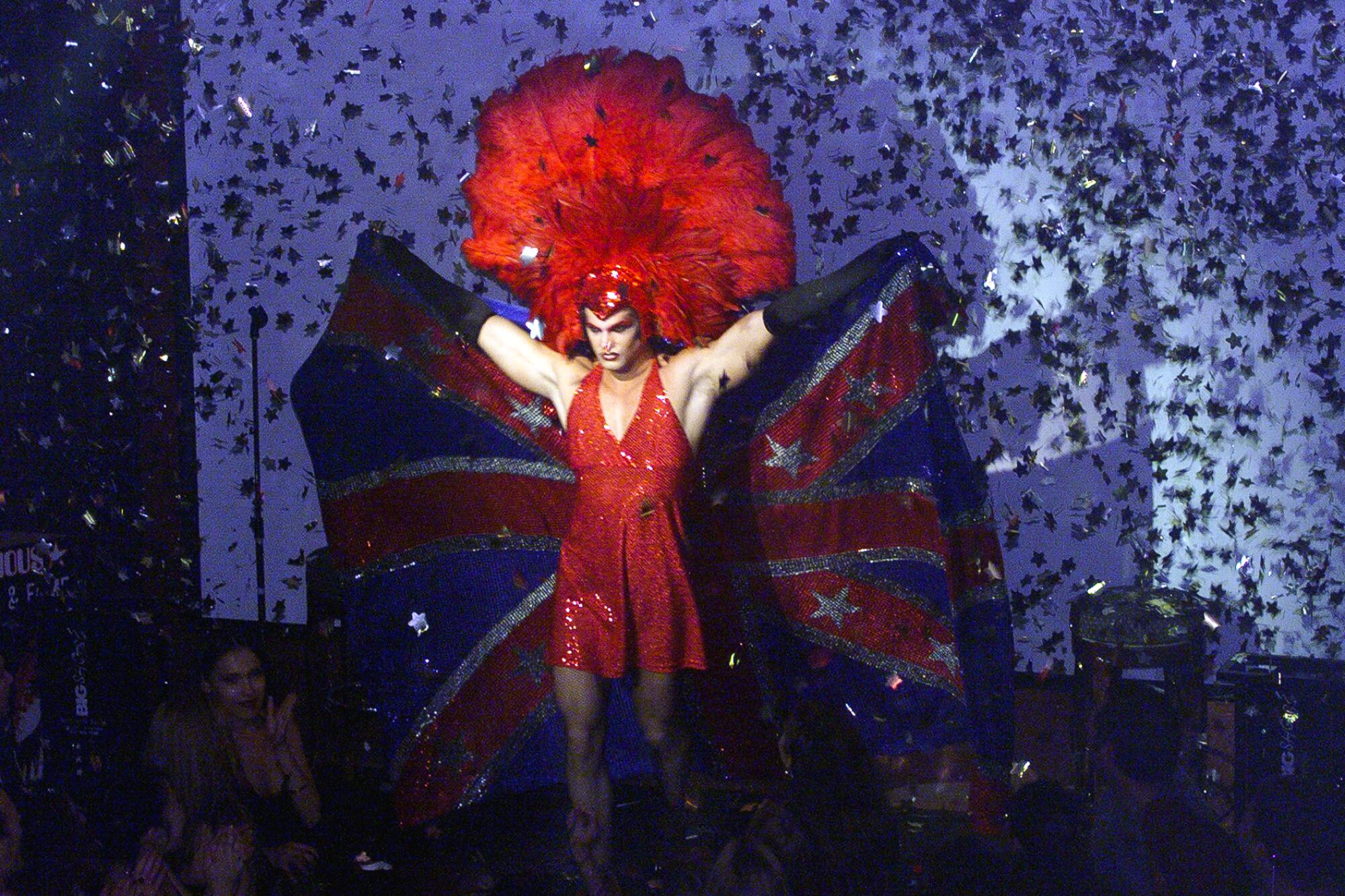 A drag performer in a red gown and large red feathered headdress onstage.