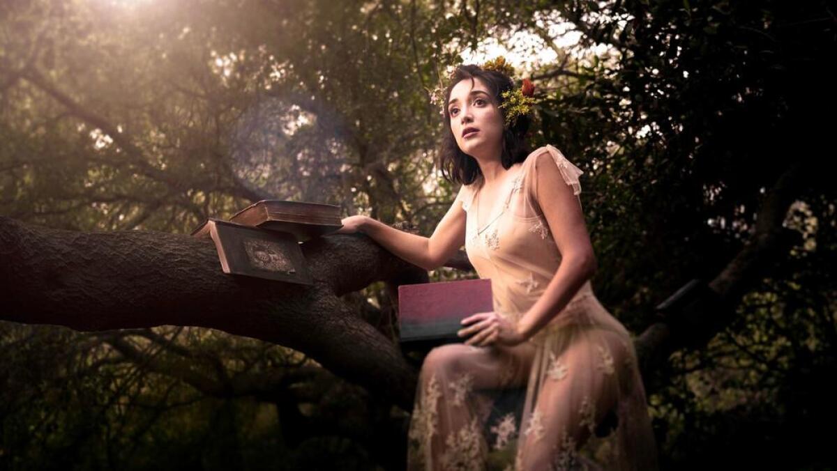 In a production of "The Tempest," an actress sits in a tree holding books.