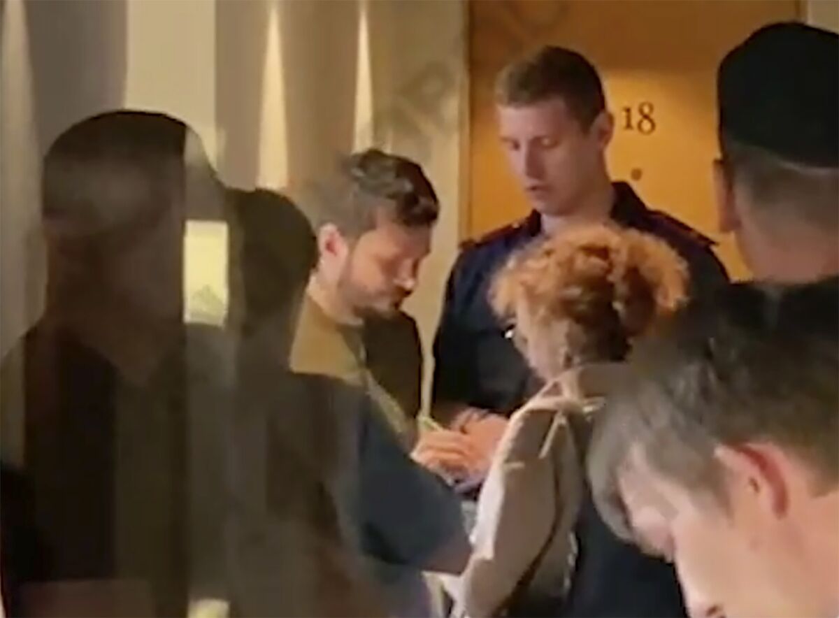 This photo taken from video provided by Ostorozhno_novosti Telegram channel, Ilya Yashin, Russian opposition activist and a municipal deputy of the Krasnoselsky district, centre left, signs a document next to his apartment in Moscow, Russia, Tuesday, July 12, 2022. Russian opposition politician Ilya Yashin was seen at a search at his apartment on Tuesday evening. According to Yashin's lawyer, the Russian Investigative Committee opened a criminal case against him of spreading deliberately false information about the Russian Army. (Ostorozhno_novosti Telegram channel via AP)