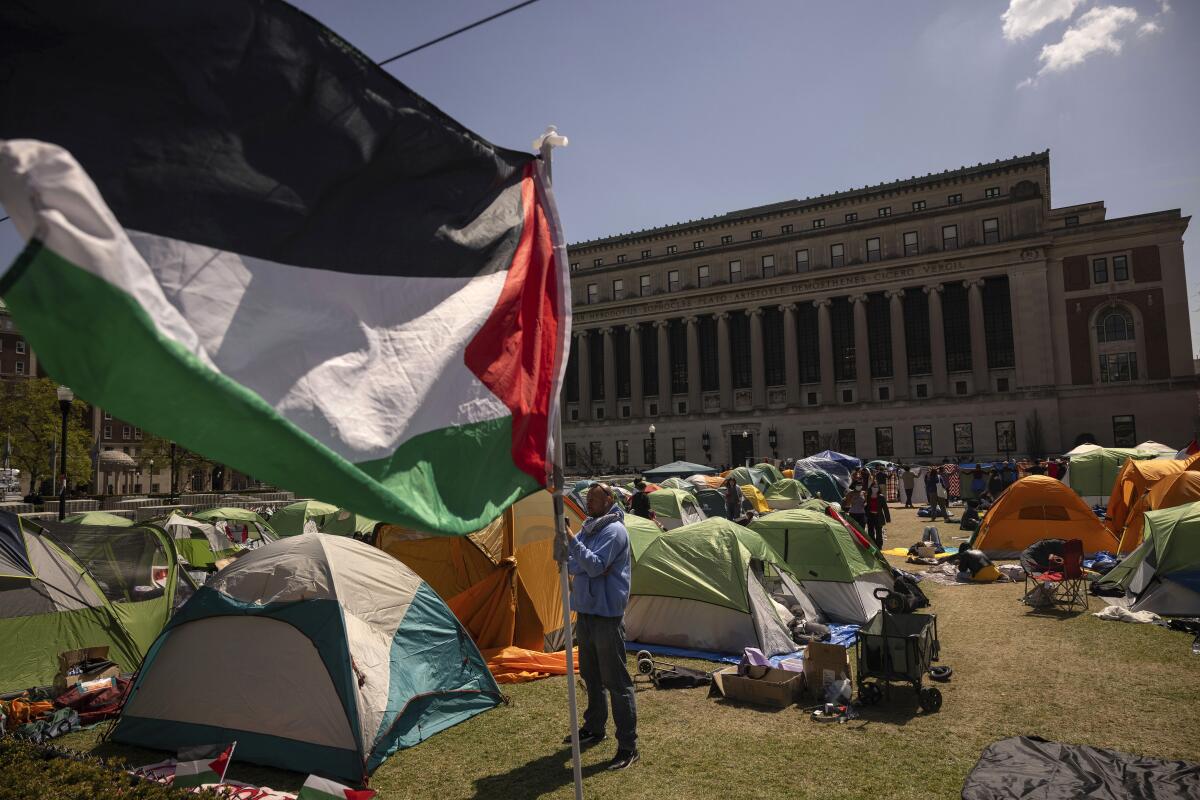 A protester holds a large Palestinian flag next to tents at Columbia University.