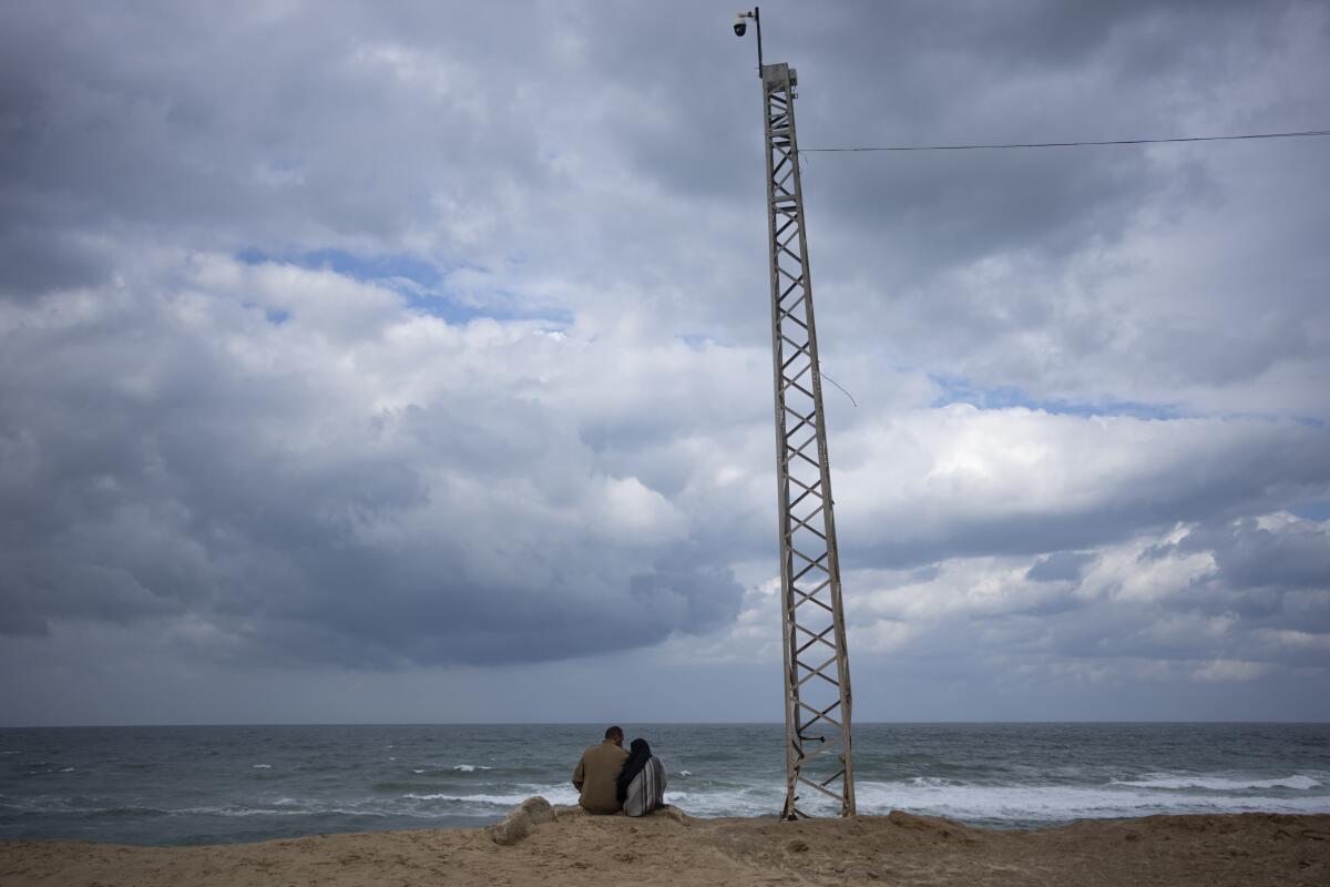 Two Palestinians displaced by the Israeli air and ground offensive on the Gaza Strip sit on the beach next to a tower.
