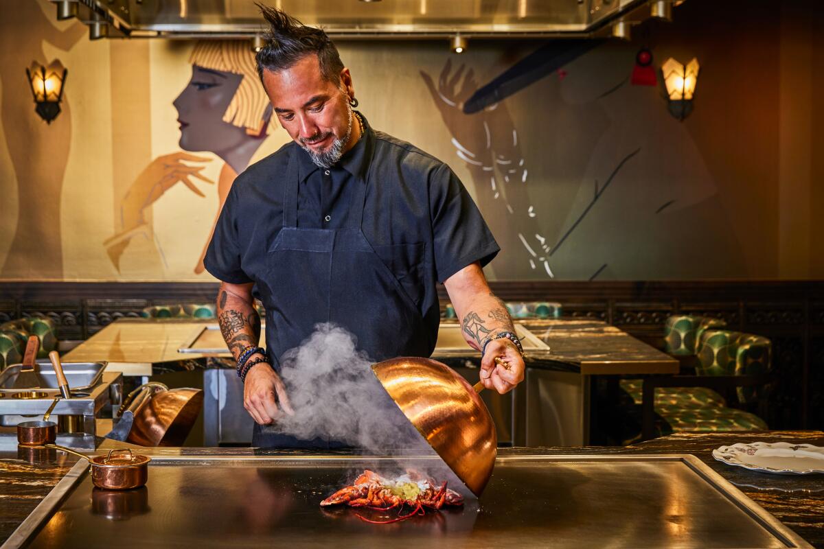 A chef stands at a teppanyaki grill, lifting a copper lid off the grill to reveal food