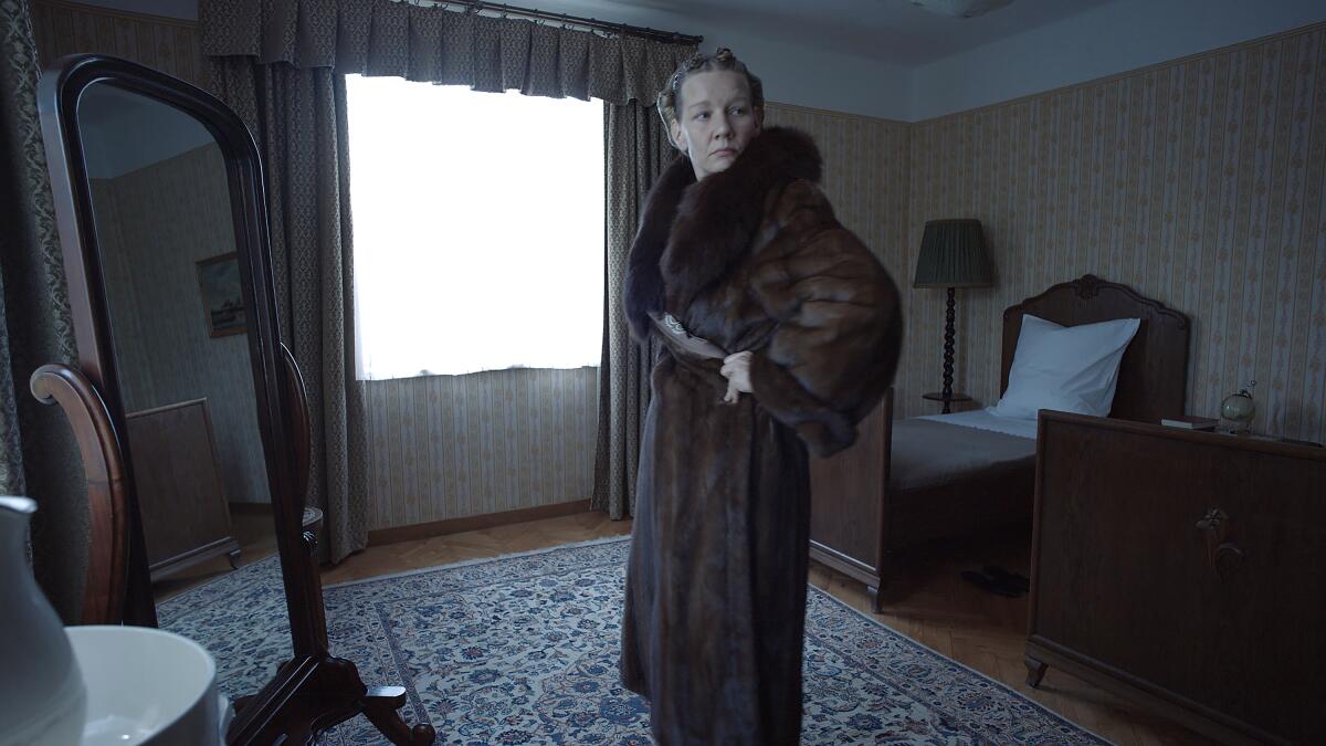 A woman tries on a fur coat, looking in the mirror.
