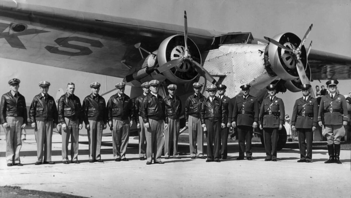 A group of men in pilot's jackets and uniforms stand in front of a plane