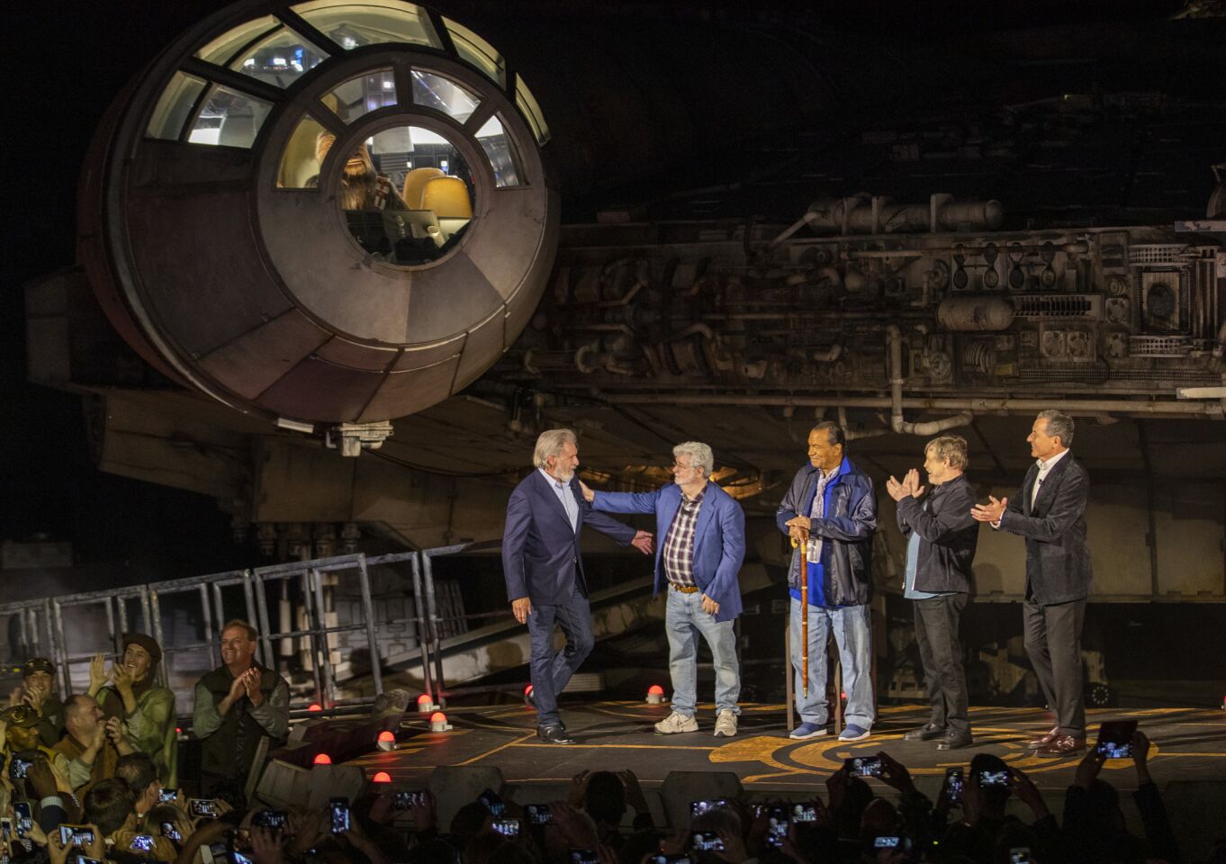 Chewbacca watches from the driver's seat as Harrison Ford, left, is greeted by George Lucas, while Billy Dee Williams, Mark Hamill and Bob Iger stand in front of the Millennium Falcon during the Star Wars: Galaxy's Edge unveiling event.