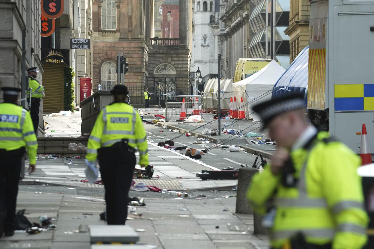 Police officers in caps and bright jackets stand alongside a road filled with debris