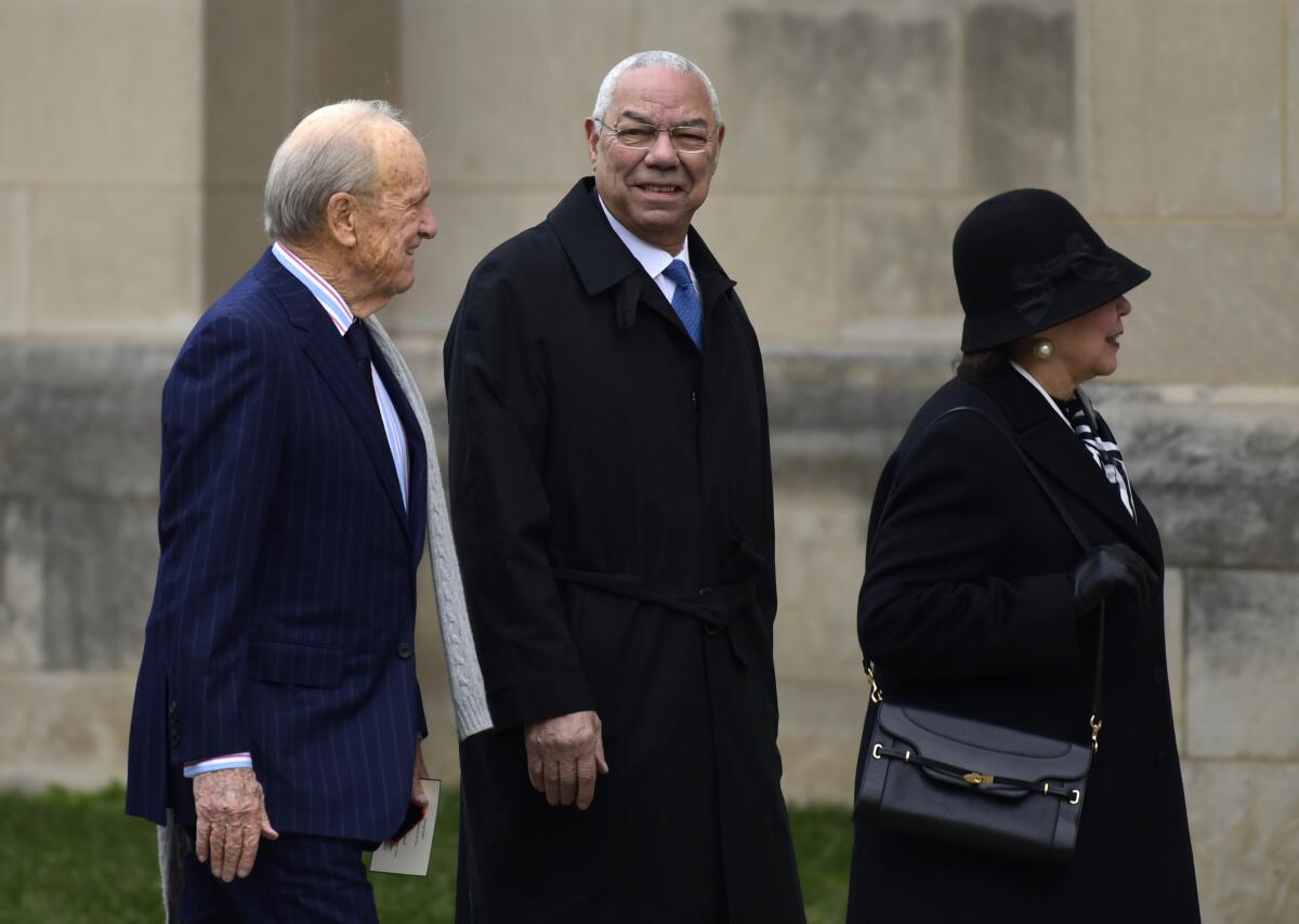 Colin Powell walks with two people outside a building