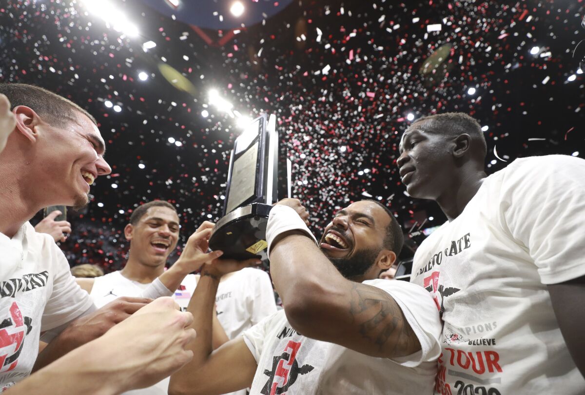 SDSU senior KJ Feagin holds up the Mountain West trophy as he, Caleb Giordano (left), Matt Mitchell (back left) and Aguek Arop (right) celebrate after the Aztecs defeated New Mexico 82-59 on Tuesday.
