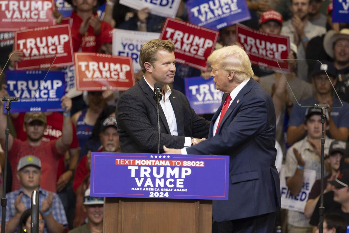 Two men shake hands at a dais in front of rally-goers.