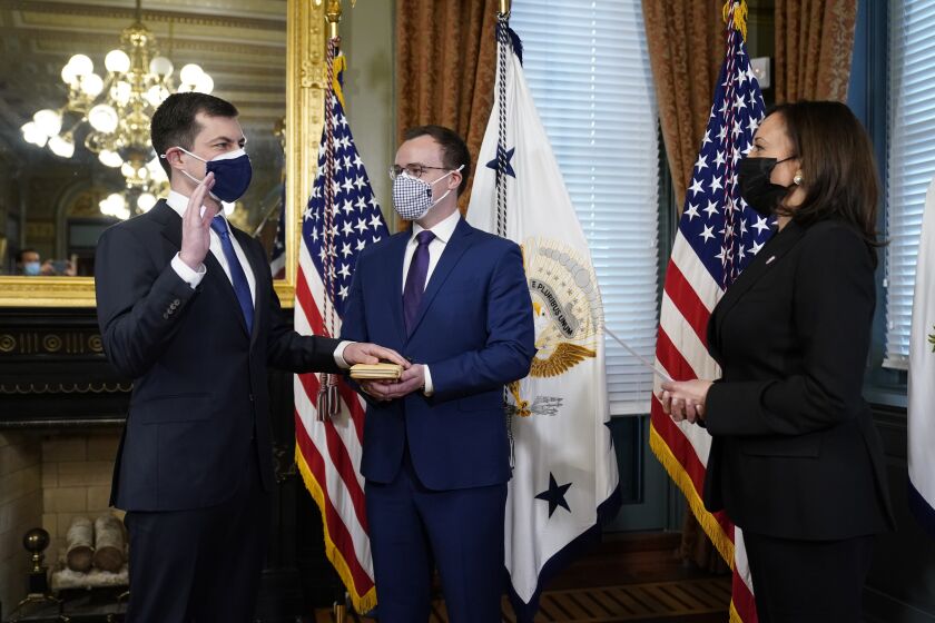 Pete Buttigieg, with his hand on the Bible held by Chasten Buttigieg, is sworn in as Transportation Secretary by Vice President Kamala Harris in the Old Executive Office Building in the White House complex in Washington, Wednesday, Feb. 3, 2021. (AP Photo/Andrew Harnik)