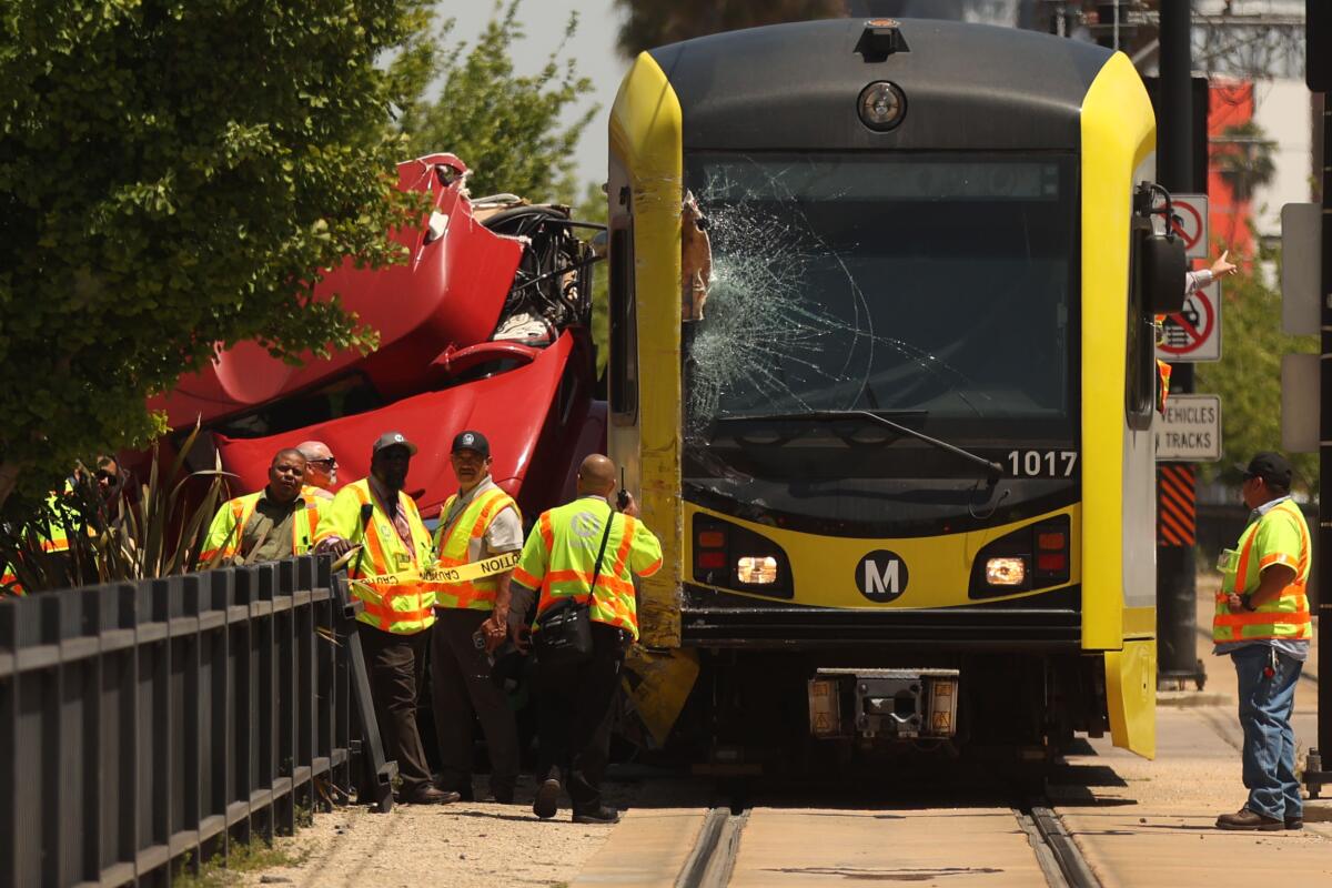 A passenger train sits on tracks near a damaged large red vehicle.