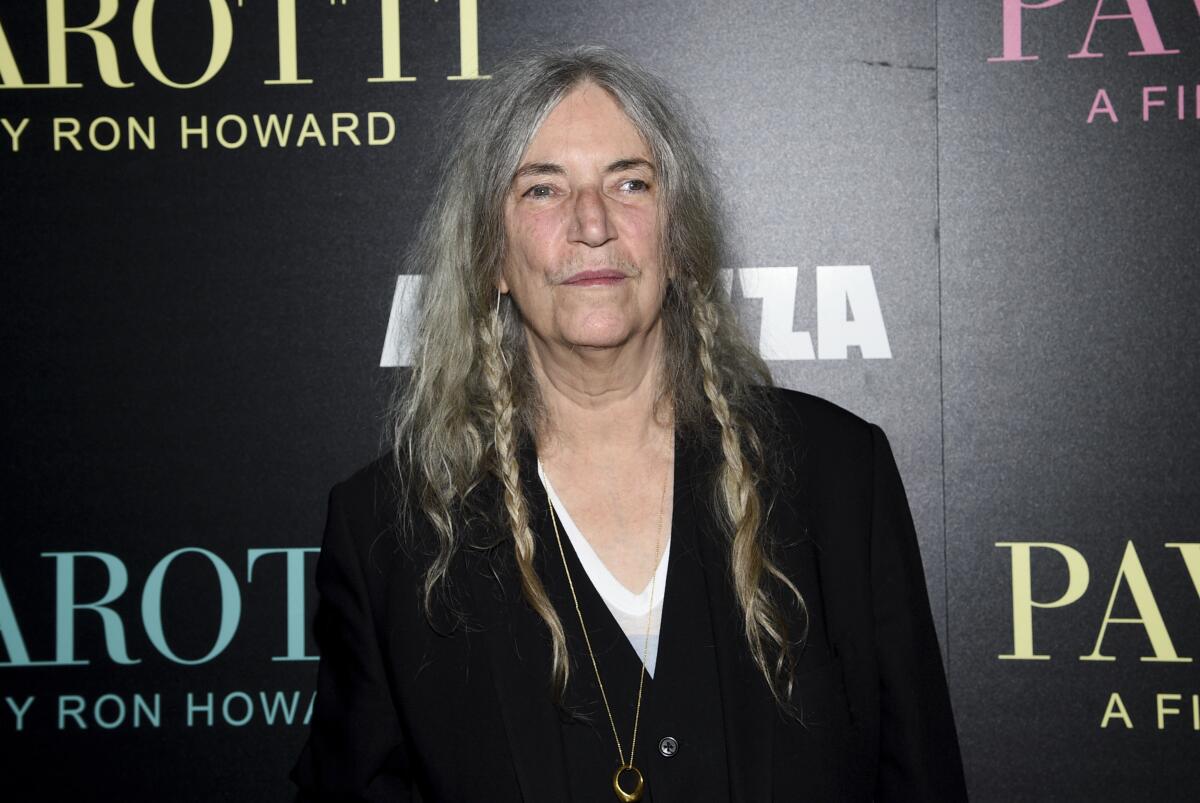 Patti Smith in a black jacket and a white shirt posing on a black background