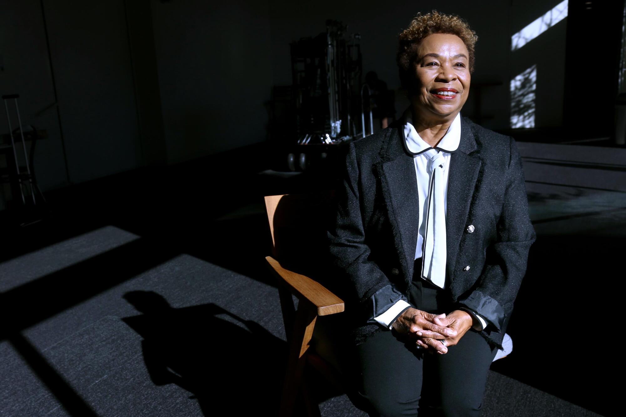 Barbara Lee sits in a chair, light beaming on her.